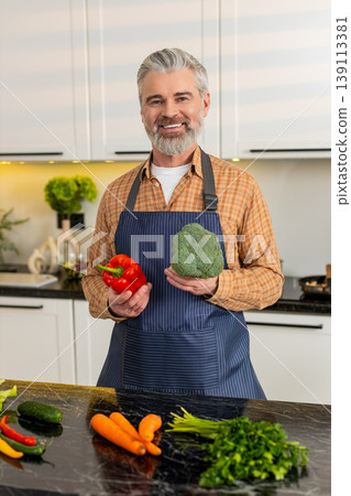 Middle-aged man smiling holding fresh pepper with broccoli for healthy diet prep at home kitchen fit Middle-aged man smiling holding fresh pepper with broccoli for healthy diet prep at home kitchen fit 139113381
