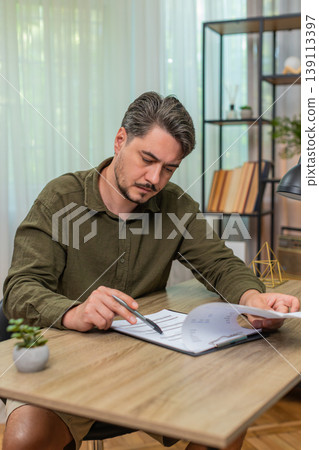 Middle-aged man reads contract thinking deeply weighing decision hesitates uncertain at table desk Middle-aged man reads contract thinking deeply weighing decision hesitates uncertain at table desk 139113397