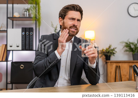 Middle-aged businessman drinks cold water winces tooth pain urgently searches dentist via smartphone Middle-aged businessman drinks cold water winces tooth pain urgently searches dentist via smartphone 139113416