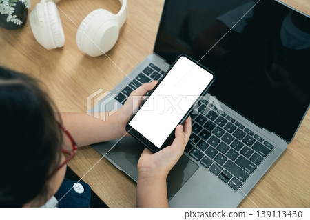 Woman Holding Smartphone in Front of Laptop on Wooden Desk with Headphones and Plant in Bright Indoor Environment Woman Holding Smartphone in Front of Laptop on Wooden Desk with Headphones and Plant in Bright Indoor Environment 139113430