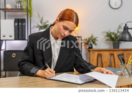 Young businesswoman carefully signs contract turning pages and securing important business agreement Young businesswoman carefully signs contract turning pages and securing important business agreement 139113454