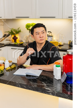 Asian man writes workout plan and records diet in journal with protein powder pills and vegetables 139113459