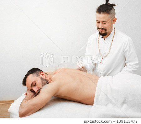 Reflexologist doing an acupuncture procedure for man with pain in his back. Acupuncture treatment of the back. Painless procedure 139113472