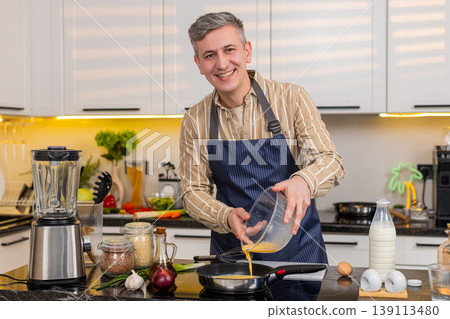Middle-aged man pouring omelet mix into frying pan while cooking healthy breakfast for diet at home Middle-aged man pouring omelet mix into frying pan while cooking healthy breakfast for diet at home 139113480