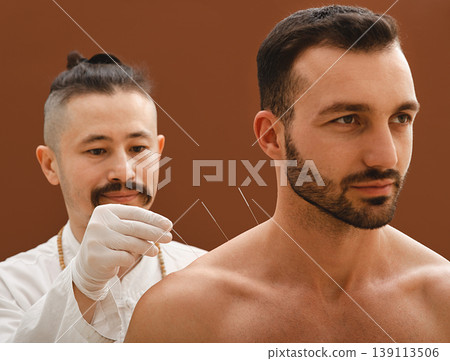 Acupuncturist inserts acupuncture needle into a man shoulder that cures him of an illness. Acupuncture treatment of diseases. Acupuncturist inserts acupuncture needle into a man shoulder that cures him of an illness. Acupuncture treatment of diseases. 139113506