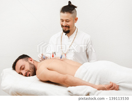 Reflexologist placing vacuum cups on the back of male patient. Health recovery using vacuum cups. Traditional oriental medicine Reflexologist placing vacuum cups on the back of male patient. Health recovery using vacuum cups. Traditional oriental medicine 139113530