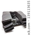 Isolated close-up view of a large, folded stack of bulk black plastic t-shirt handle bags. 139113635