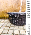 Close up of water pouring into a black plastic basin and overflowing onto the tiled floor. 139113637