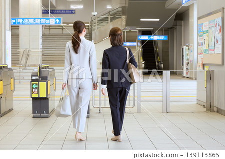 兩名身穿職業套裝的職業婦女的背影正走過火車站的檢票口。 兩名身穿職業套裝的職業婦女的背影正走過火車站的檢票口。 139113865