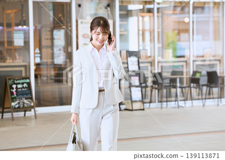 一位身穿白色職業套裝的年輕女商務人士一邊打電話一邊走在城市裡——這是銷售人員在辦公室外工作的畫面。 一位身穿白色職業套裝的年輕女商務人士一邊打電話一邊走在城市裡——這是銷售人員在辦公室外工作的畫面。 139113871