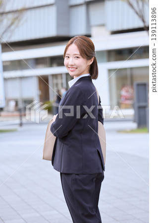 一位面帶微笑的年輕女商人走過辦公區；一位身穿海軍藍西裝的日本上班族正在通勤上班。 139113896