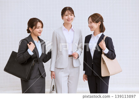 三位年輕的女上班族在商業區聊天;身著職業套裝的日本職業婦女通勤。 三位年輕的女上班族在商業區聊天;身著職業套裝的日本職業婦女通勤。 139113897
