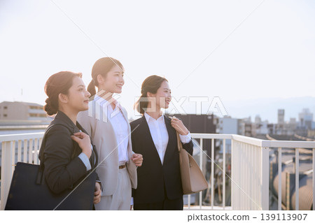 早晨通勤場景:三位年輕的職業女性在戶外人行天橋上面帶著樂觀的微笑;一位身穿西裝的新員工。 早晨通勤場景:三位年輕的職業女性在戶外人行天橋上面帶著樂觀的微笑;一位身穿西裝的新員工。 139113907