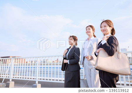 三位身著職業套裝的年輕女商人走在橋上,面向藍天。 三位身著職業套裝的年輕女商人走在橋上,面向藍天。 139113912