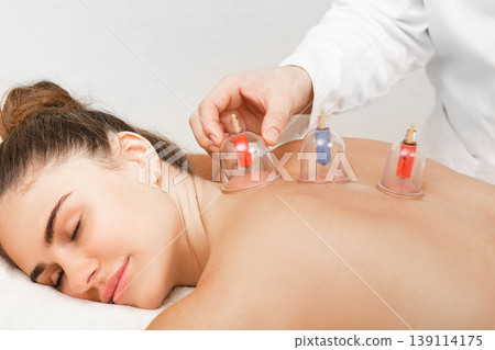 Traditional Chinese medicine doctor doing massage with vacuum cups to a female patient. Acupuncture cups close-up Traditional Chinese medicine doctor doing massage with vacuum cups to a female patient. Acupuncture cups close-up 139114175