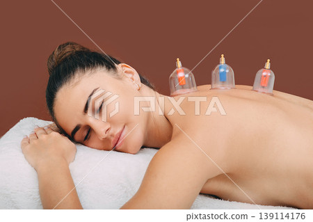 Traditional oriental medicine. Health recovery woman with vacuum cups. Closeup of vacuum cups on woman's back on brown background Traditional oriental medicine. Health recovery woman with vacuum cups. Closeup of vacuum cups on woman's back on brown background 139114176