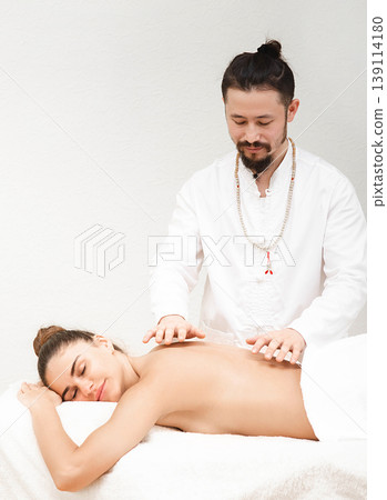 Doctor of traditional oriental medicine doing non contact energetic massage to a beautiful woman in a spa salon. The body is cleansed of negative energy. Reiki massage Doctor of traditional oriental medicine doing non contact energetic massage to a beautiful woman in a spa salon. The body is cleansed of negative energy. Reiki massage 139114180