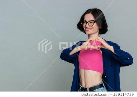 Woman making heart shape with fingers looking gently at left side expressing love affection caring Woman making heart shape with fingers looking gently at left side expressing love affection caring 139114739