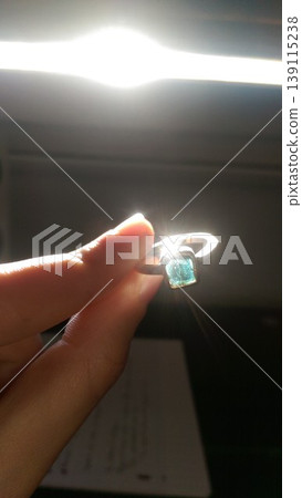 Phone photo of a female hand holding an artisan silver ring with a blue cracked sapphire. Casual jewelry scene showing craftsmanship, detail, and personal style. Phone photo of a female hand holding an artisan silver ring with a blue cracked sapphire. Casual jewelry scene showing craftsmanship, detail, and personal style. 139115238