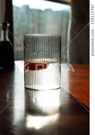 Cinematic close-up of fluted water glass with lemon slice on wooden table. Soft morning sunlight, shadow play, minimalist aesthetic, elegant glassware Cinematic close-up of fluted water glass with lemon slice on wooden table. Soft morning sunlight, shadow play, minimalist aesthetic, elegant glassware 139115397