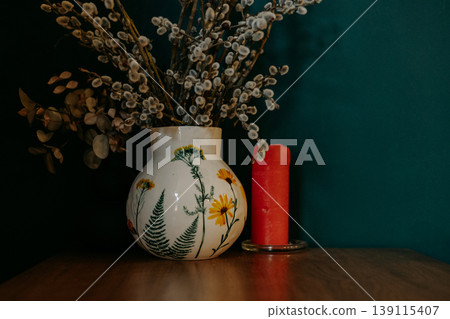 Spring interior still life with pussy willow branches in floral ceramic vase and red candle. Moody aesthetic, farmhouse decor, artisanal pottery, easter atmosphere, cozy home styling on dark teal. Spring interior still life with pussy willow branches in floral ceramic vase and red candle. Moody aesthetic, farmhouse decor, artisanal pottery, easter atmosphere, cozy home styling on dark teal. 139115407