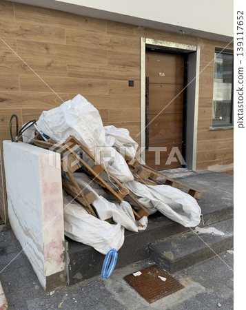 Pile of wooden pallets and bags on pavement outside a building under renovation Pile of wooden pallets and bags on pavement outside a building under renovation 139117652