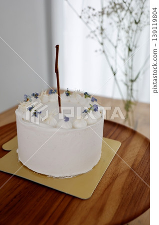 A birthday cake to celebrate a child's first birthday. Decorated with the number 1. White cream. Small purple flowers. Wooden table. 139119804