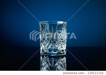 Empty crystal glass on a black reflective background, with blue lighting. Empty crystal glass on a black reflective background, with blue lighting. 139121316