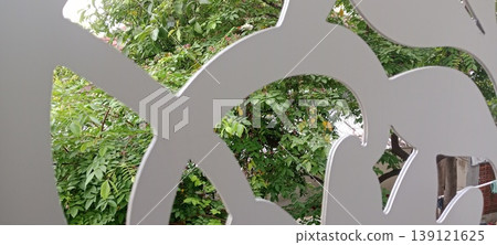 View of green foliage through decorative laser cut panel with abstract pattern View of green foliage through decorative laser cut panel with abstract pattern 139121625