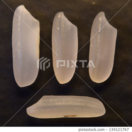 Four grains of uncooked rice, isolated on a dark background. 139121767