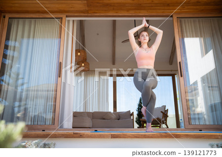 Young woman practicing Yoga Eagle pose on modern home terrace Young woman practicing Yoga Eagle pose on modern home terrace 139121773