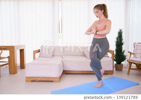 Young woman practicing eagle pose yoga on mat in living room Young woman practicing eagle pose yoga on mat in living room 139121789