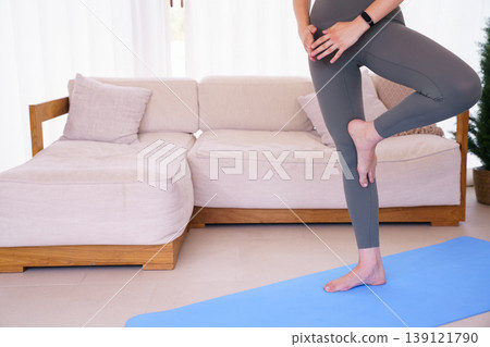 Young woman in sports bra practicing tree pose yoga at home 139121790