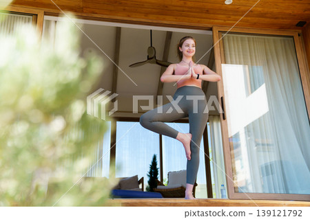 Young woman practicing tree pose yoga on home terrace 139121792