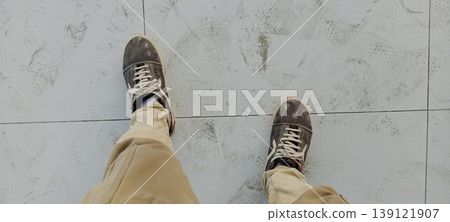 Top View of Person Wearing Dirty Sneakers and Beige Pants Standing on White Marble Tile Floor Top View of Person Wearing Dirty Sneakers and Beige Pants Standing on White Marble Tile Floor 139121907