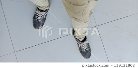 Top View of Person Wearing Dirty Sneakers and Beige Pants Standing on White Marble Tile Floor Top View of Person Wearing Dirty Sneakers and Beige Pants Standing on White Marble Tile Floor 139121908