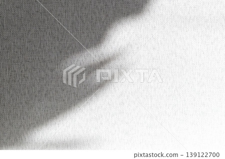 A textured white fabric, linen or a similar woven material, with a soft grey shadow cast across the upper left portion A textured white fabric, linen or a similar woven material, with a soft grey shadow cast across the upper left portion 139122700