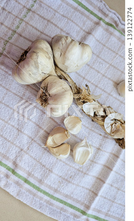 Vertical close up of dried garlic braid with whole garlic bulbs and loose cloves on checkered linen towel, warm rustic food styling Vertical close up of dried garlic braid with whole garlic bulbs and loose cloves on checkered linen towel, warm rustic food styling 139122774