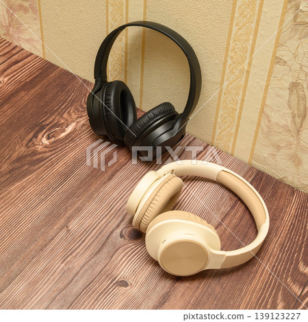 black headphones in the background and beige ones in the foreground on a wooden table black headphones in the background and beige ones in the foreground on a wooden table 139123227