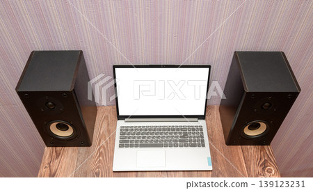 gray laptop with a bright white screen on a wooden table between two black audio speakers gray laptop with a bright white screen on a wooden table between two black audio speakers 139123231