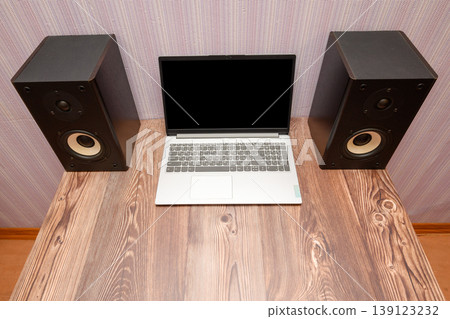 open gray laptop with a turned off black screen on a table between two large speakers open gray laptop with a turned off black screen on a table between two large speakers 139123232