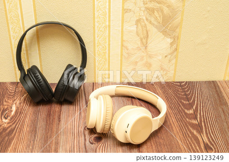 black headphones stand vertically and beige ones lie on a wooden table near the wall black headphones stand vertically and beige ones lie on a wooden table near the wall 139123249
