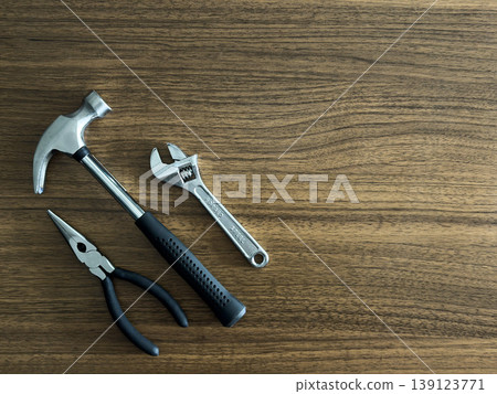 Hammer Pliers and Adjustable Wrench Flat Lay on Wooden Table DIY Repair Tools Home Improvement Construction Workshop Maintenance Hardware Background 139123771