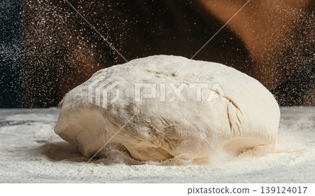 Raw bread dough with flying flour particles on dark background artisan baking process close up food texture Raw bread dough with flying flour particles on dark background artisan baking process close up food texture 139124017
