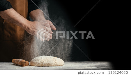 Baker clapping flour over dough with falling flour particles and copy space Baker clapping flour over dough with falling flour particles and copy space 139124030