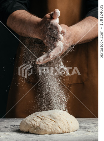 Baker clapping hands with flour dust over dough, bread making action close up Baker clapping hands with flour dust over dough, bread making action close up 139124035