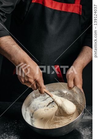 Baker mixing elastic dough in metal bowl with spoon homemade baking process 139124037