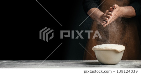 Baker clapping hands with flour over rising dough in bowl on dark background 139124039