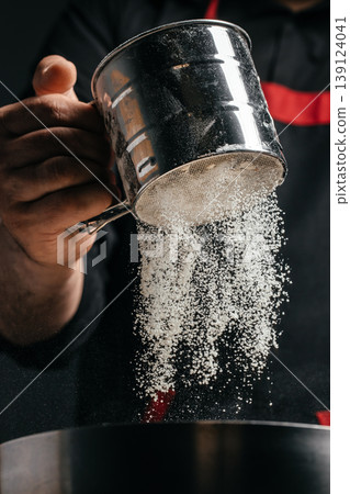 Sifting flour through metal sieve into bowl dramatic baking process close up 139124041