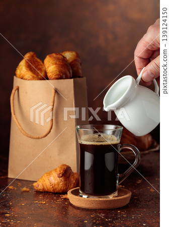 Coffee latte and paper bag with croissants on a brown background. Coffee latte and paper bag with croissants on a brown background. 139124150
